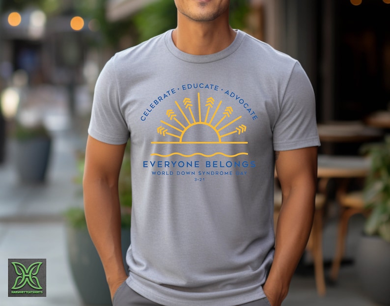 May include: A gray t-shirt with a blue and yellow graphic design. The graphic features a stylized sun with rays and the text "Celebrate, Educate, Advocate. Everyone Belongs. World Down Syndrome Day 3-21".