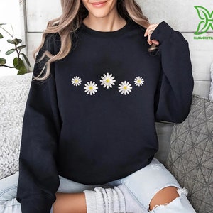 a woman sitting on a couch wearing a black sweatshirt with daisies on it