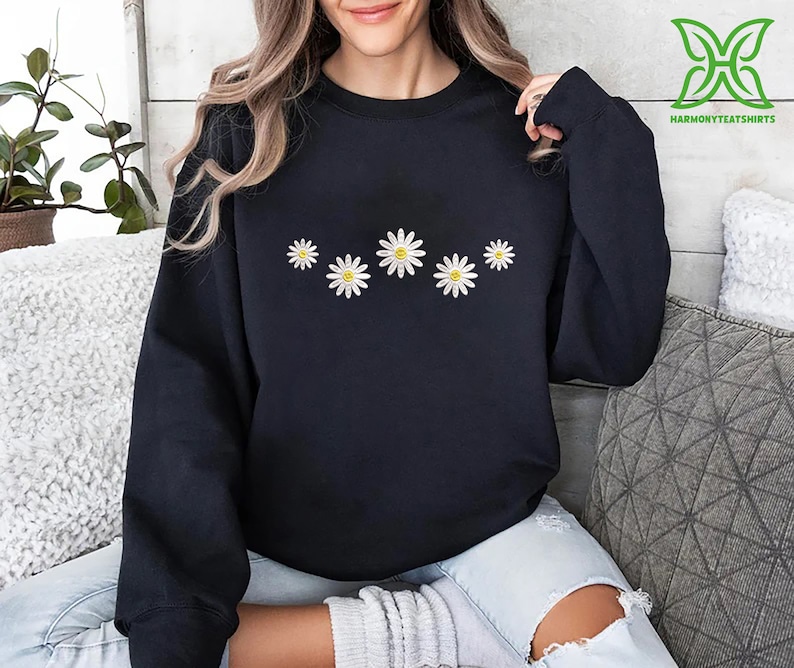 a woman sitting on a couch wearing a black sweatshirt with daisies on it
