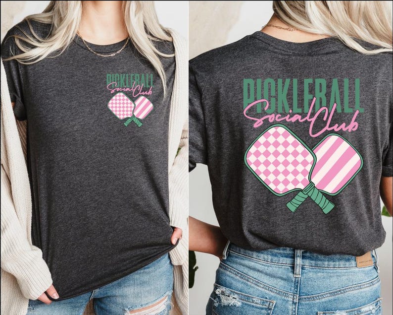 Op de afbeelding: Een donkergrijs T-shirt met een roze en groen pickleball-paddle ontwerp en de tekst "Pickleball Social Club" in groen.