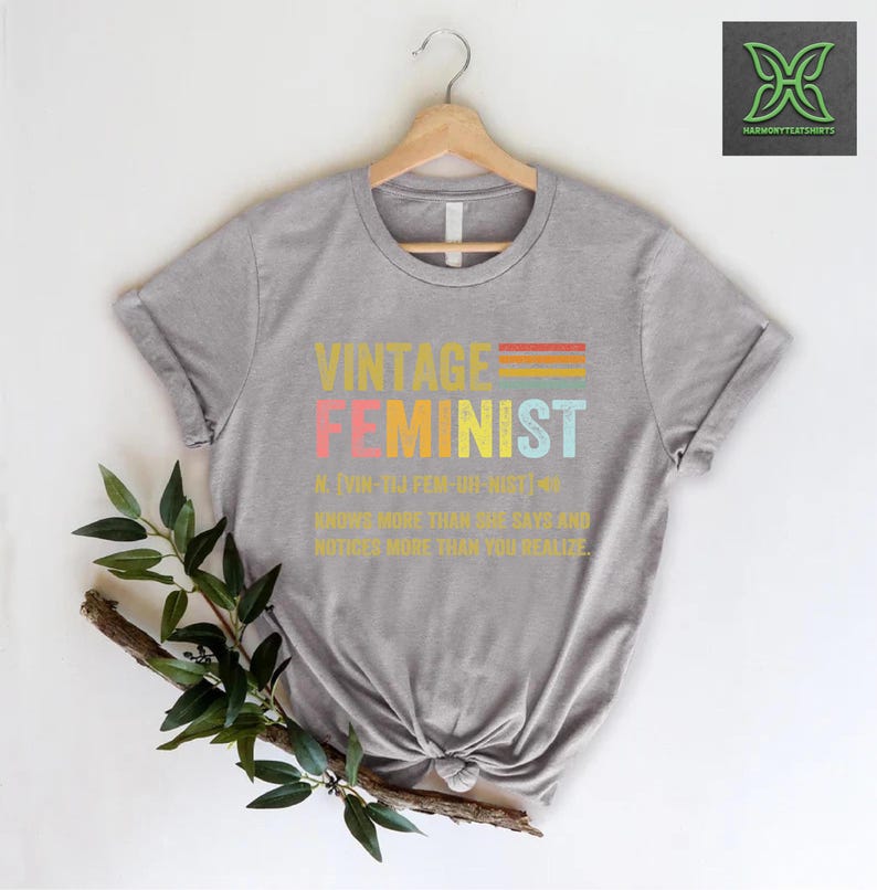 May include: Gray t-shirt with a vintage-style graphic that reads "Vintage Feminist" and a definition of the word. The graphic is in rainbow colors.