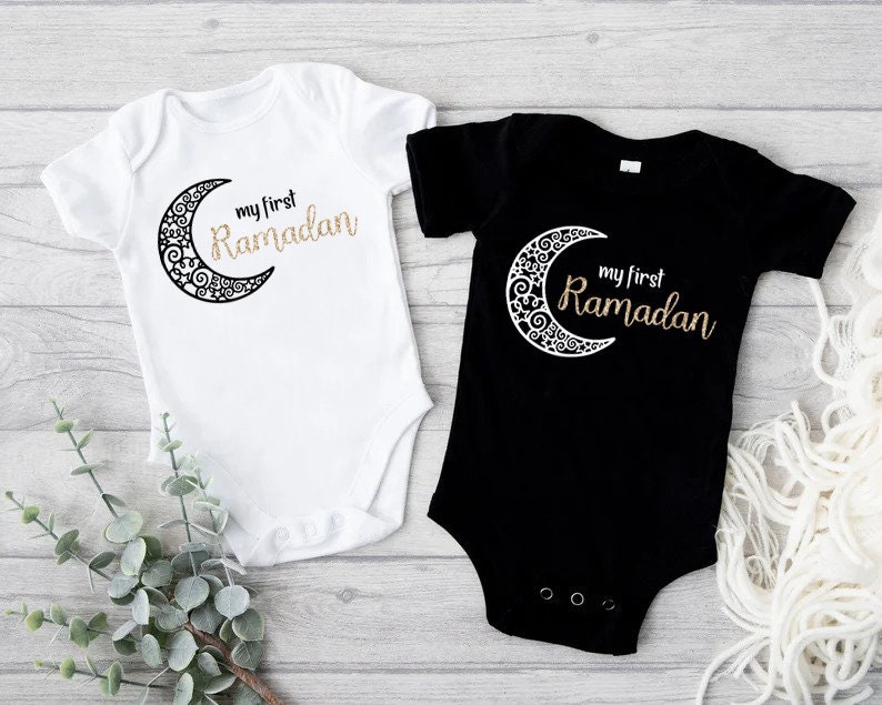 One white and one black baby onesie for Ramadan with a crescent moon and text