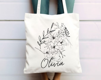 May include: White canvas tote bag with black floral design and the name Olivia printed on the front.