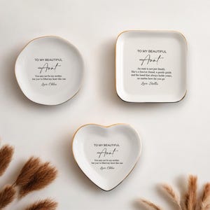 May include: Three white ceramic trinket dishes with gold trim. Each dish has a different shape: round, square, and heart. The dishes have a message for an aunt, with the text "To my beautiful Aunt".