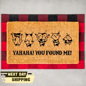 May include: A brown coir doormat with a black and white design of five cartoon characters and the text "YAHAHA! YOU FOUND ME!"