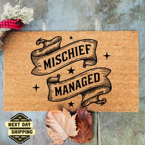 May include: A brown coir doormat with the text "Mischief Managed" in black lettering on two vintage-style banners.
