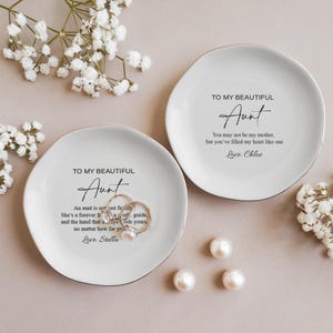 May include: Two white ceramic ring dishes with gold trim. The dishes have a message for an aunt, "To my beautiful Aunt." One dish says, "An aunt is not just family, she's a forever friend, a constant guide, and the hand that always holds yours, no matter how far you are." The other dish says, "You may not be my mother, but you've filled my heart like one."