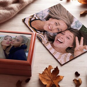 May include: Two wooden boxes with a photo of two women smiling at the camera. The photo in the smaller box is a close-up of the women, while the photo in the larger box is a wider shot of the women lying on the ground.