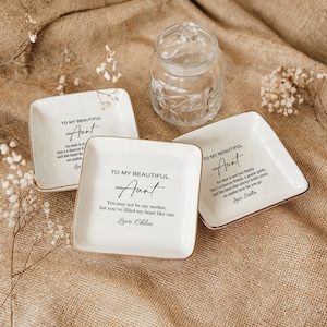 May include: Three white ceramic ring dishes with gold trim. Each dish has a different message for an aunt. The messages are: "To my beautiful Aunt, An aunt is not just family...", "To my beautiful Aunt, You may not be my mother...", and "To my beautiful Aunt, An aunt is not just family..."