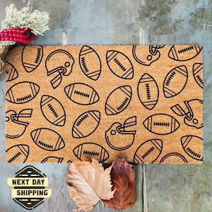 May include: A brown coir doormat with a pattern of black footballs and helmets. The doormat has the words "Next Day Shipping" printed on it.