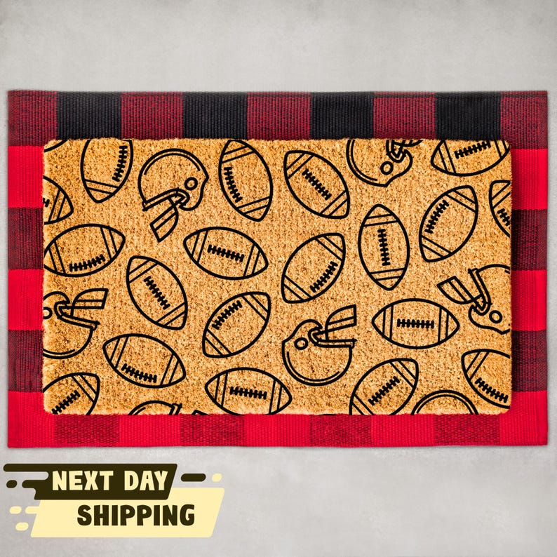 May include: A brown coir doormat with a red and black chequered border. The doormat has a pattern of black footballs and helmets.