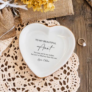 May include: White heart-shaped trinket dish with a gold rim. The dish has a message that reads "To my beautiful Aunt You may not be my mother, but you've filled my heart like one Love. Chloe"