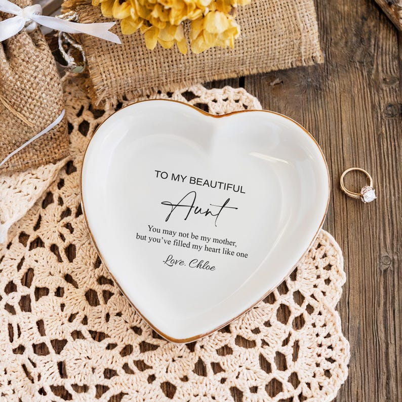 May include: White heart-shaped trinket dish with a gold rim. The dish has a message that reads "To my beautiful Aunt You may not be my mother, but you've filled my heart like one Love. Chloe"
