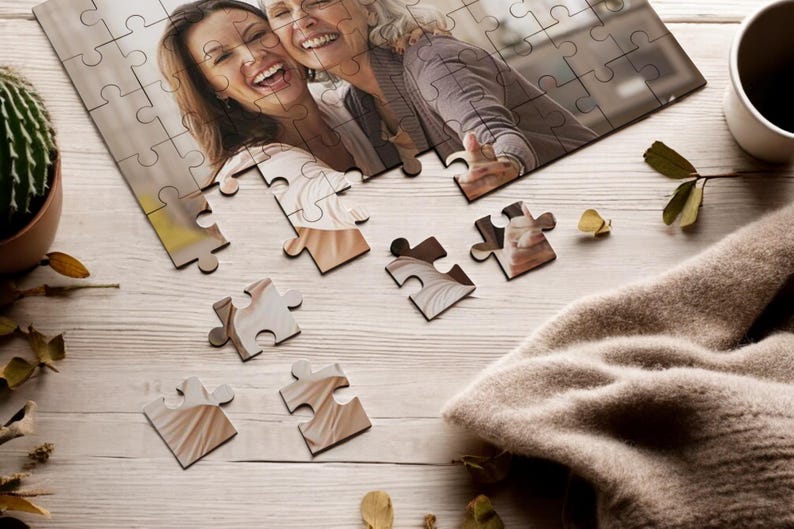 May include: A partially completed jigsaw puzzle on a wooden table with a brown sweater, a potted cactus, and a cup of coffee. The puzzle features a photo of two women smiling.