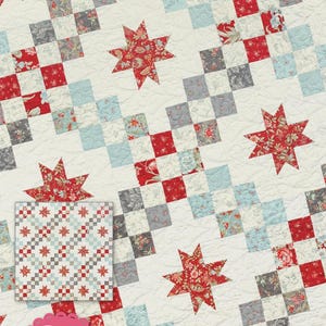 May include: A patchwork quilt featuring a repeating pattern of red floral stars and squares in red, grey, and light blue. The words "Castle Courtyard" are at the top. Designed by Jocelyn Ueng.