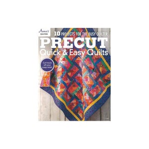 May include: A book cover with the title "Precut Quick & Easy Quilts" featuring a colorful quilt with a geometric pattern. The book cover is blue, yellow, and white with the text "Annie's Quilting" in the top left corner.