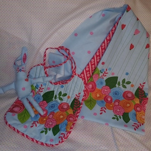 May include: A light blue baby bib, bunny toy, and hooded towel set. The set features a floral pattern with pink, orange, and blue flowers. The bib has a red and white striped trim, and the bunny toy is light blue.