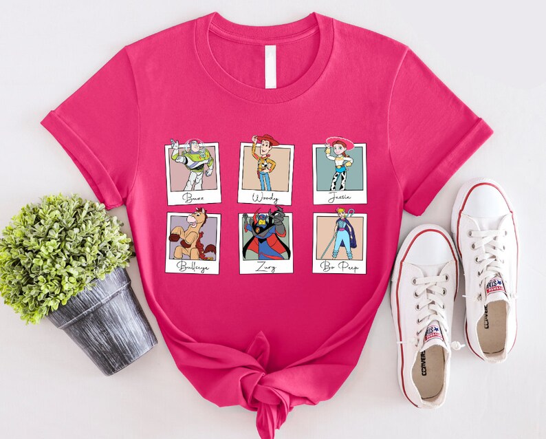 Puede incluir: Camiseta rosa con un gr&aacute;fico de seis personajes de Toy Story en marcos Polaroid. Los personajes son Buzz Lightyear, Woody, Jessie, Bullseye, Zurg y Bo Peep. El texto debajo de cada personaje dice "Buzz", "Woody", "Jessie", "Bullseye", "Zurg" y "Bo Peep".