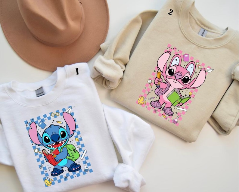 Puede incluir: Dos sudaderas, una blanca y otra beige, cada una con un personaje de dibujos animados. La sudadera blanca tiene un personaje azul con un libro rojo y una mochila verde. La sudadera beige tiene un personaje rosa con un libro verde y un l&aacute;piz.