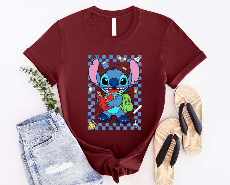 Puede incluir: Camiseta granate con una ilustraci&oacute;n de dibujos animados de Stitch de Lilo & Stitch. Stitch sostiene un libro y lleva una mochila, sobre un fondo a cuadros azules y blancos. La imagen incluye un par de chanclas.