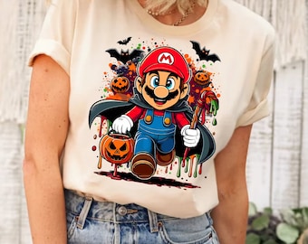 Może przedstawiać: Biały t-shirt z kolorową grafiką przedstawiającą Mario przebranego za wampira, trzymającego laskę cukrową i wiaderko na dynie. Grafika jest otoczona nietoperzami i dyniami.