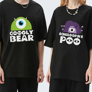 Puede incluir: Dos camisetas negras con un estampado gráfico de personajes de la película Monsters Inc. La camiseta de la izquierda dice "Coogly Bear" y presenta un monstruo verde con un ojo. La camiseta de la derecha dice "Schmoopsie Poo" y presenta un monstruo morado con un ojo.