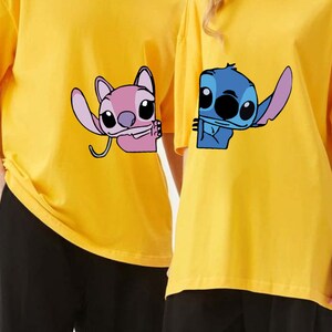K&ouml;nnte beinhalten: Zwei gelbe T-Shirts mit Cartoon-Charakteren. Eines zeigt einen pinkfarbenen Charakter, der winkt, das andere einen blauen Charakter. Beide haben kurze &Auml;rmel und eine lockere Passform, ideal f&uuml;r den Alltag. Die T-Shirts sind leuchtend gelb.