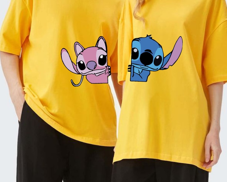 K&ouml;nnte beinhalten: Zwei gelbe T-Shirts mit Cartoon-Charakteren. Eines zeigt einen pinkfarbenen Charakter, der winkt, das andere einen blauen Charakter. Beide haben kurze &Auml;rmel und eine lockere Passform, ideal f&uuml;r den Alltag. Die T-Shirts sind leuchtend gelb.