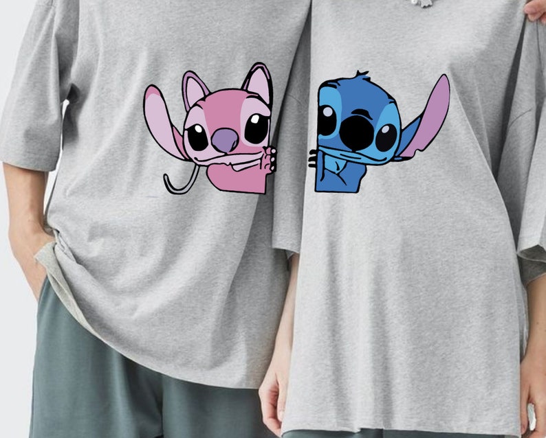 K&ouml;nnte beinhalten: Zwei graue T-Shirts mit Cartoon-Charakteren. Eines zeigt einen rosa Charakter mit gro&szlig;em Ohr, das andere einen blauen Charakter. Beide Charaktere l&auml;cheln. Die T-Shirts haben kurze &Auml;rmel.