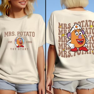 May include: A white t-shirt featuring a brown graphic of Mrs. Potato Head from Toy Story. The graphic includes the text "MRS. POTATO" and "EST. 1995 TOY STORY".