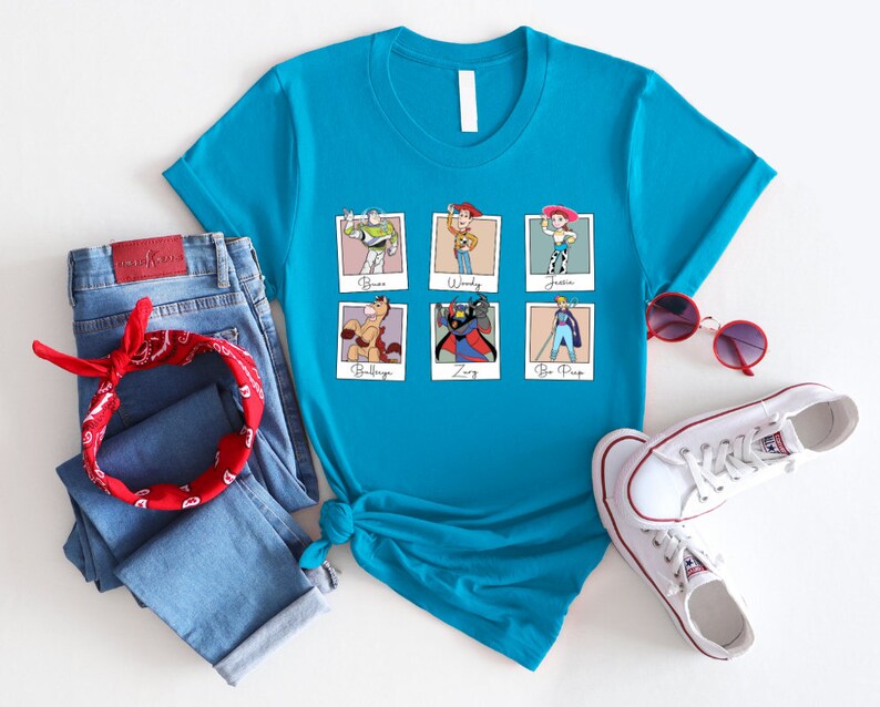 Puede incluir: Una camiseta azul turquesa con un gr&aacute;fico de seis personajes de Toy Story en marcos Polaroid. Los personajes son Buzz Lightyear, Woody, Jessie, Bullseye, Zurg y Bo Peep. El texto debajo de cada marco identifica al personaje.