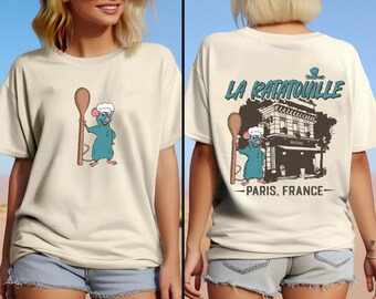 May include: Two white t-shirts featuring a graphic print of Remy the rat from the film Ratatouille. One shirt depicts Remy holding a wooden spoon and wearing a chef's hat. The other shirt shows a graphic of the restaurant 'La Ratatouille' in Paris, France.