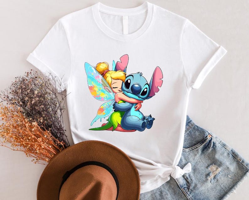 K&ouml;nnte beinhalten: Wei&szlig;es T-Shirt mit einem bunten Cartoon-Bild von Tinkerbell, die Stitch umarmt. Stitch ist blau mit einem rosa Ohr und einer rosa Nase. Tinkerbell hat blonde Haare und ein gr&uuml;nes Kleid.