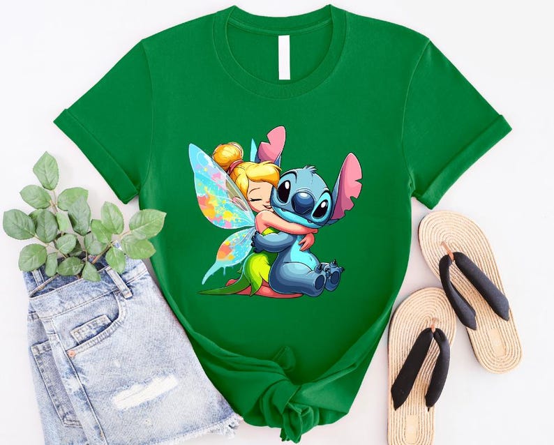 K&ouml;nnte beinhalten: Gr&uuml;nes T-Shirt mit einem Cartoon-Bild von Stitch aus Lilo & Stitch, der Tinkerbell aus Peter Pan umarmt. Stitch ist blau und Tinkerbell tr&auml;gt ein gr&uuml;nes Kleid mit Feenfl&uuml;geln.
