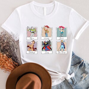 Puede incluir: Camiseta blanca con un gr&aacute;fico de seis personajes de Toy Story en marcos Polaroid. Los personajes son Buzz Lightyear, Woody, Jessie, Bullseye, Zurg y Bo Peep.