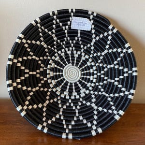 Pu&ograve; includere: Appeso a parete in tessuto nero e bianco con un design circolare. Il design presenta cerchi concentrici e linee radianti.