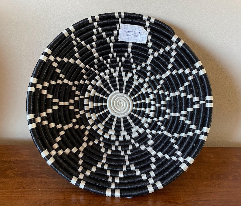 Pu&ograve; includere: Appeso a parete in tessuto nero e bianco con un design circolare. Il design presenta cerchi concentrici e linee radianti.