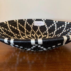 Pu&ograve; includere: Un cesto rotondo intrecciato in bianco e nero. Il cesto &egrave; fatto di fibre naturali e ha un motivo geometrico.