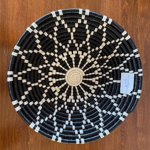 Pu&ograve; includere: Un cesto intrecciato bianco e nero con un design circolare. Il cesto &egrave; fatto di materiali naturali e ha un aspetto rustico.