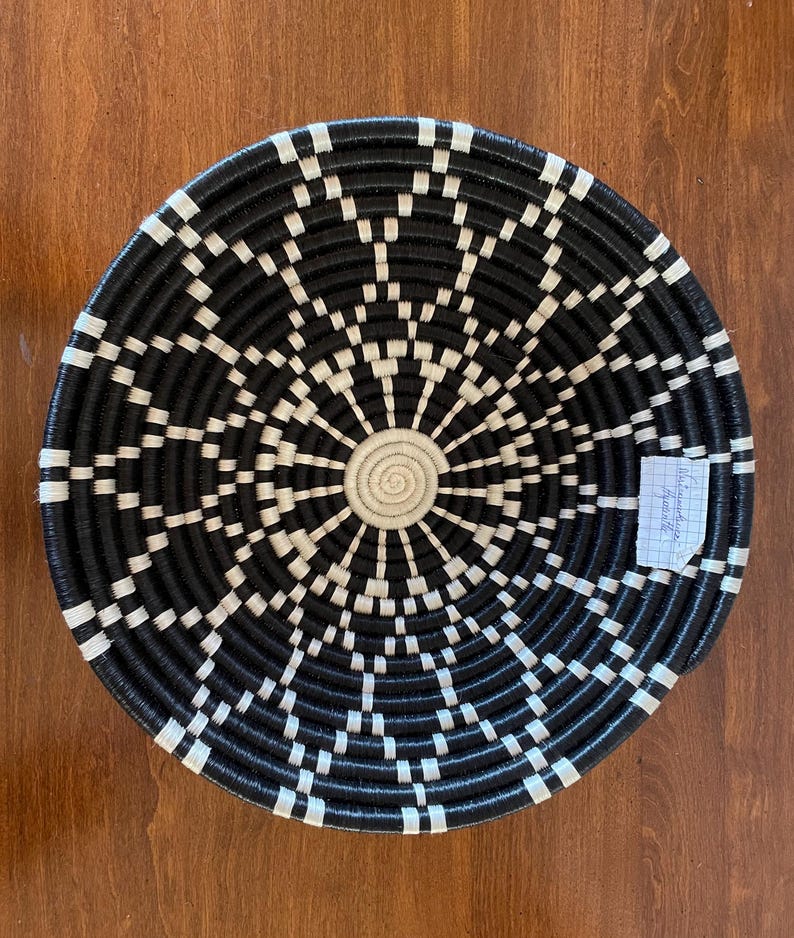 Pu&ograve; includere: Un cesto intrecciato bianco e nero con un design circolare. Il cesto &egrave; fatto di materiali naturali e ha un aspetto rustico.
