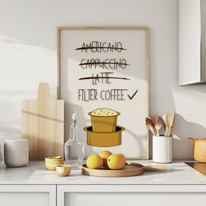 May include: A white framed print with a black checkmark next to the text "Filter Coffee" and a line through the words "Americano", "Cappuccino", and "Latte". The print also features a cartoon illustration of a coffee filter with coffee grounds.