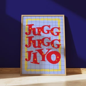May include: Framed art print featuring the words "JUGG JUGG Jiyo" in red, outlined in white, with yellow star accents. The text is on a light blue grid background, framed by a yellow border, and set against a dark blue wall.