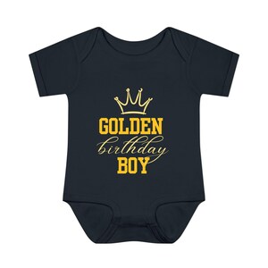 May include: A dark blue baby onesie with a gold crown and the text "GOLDEN birthday BOY".