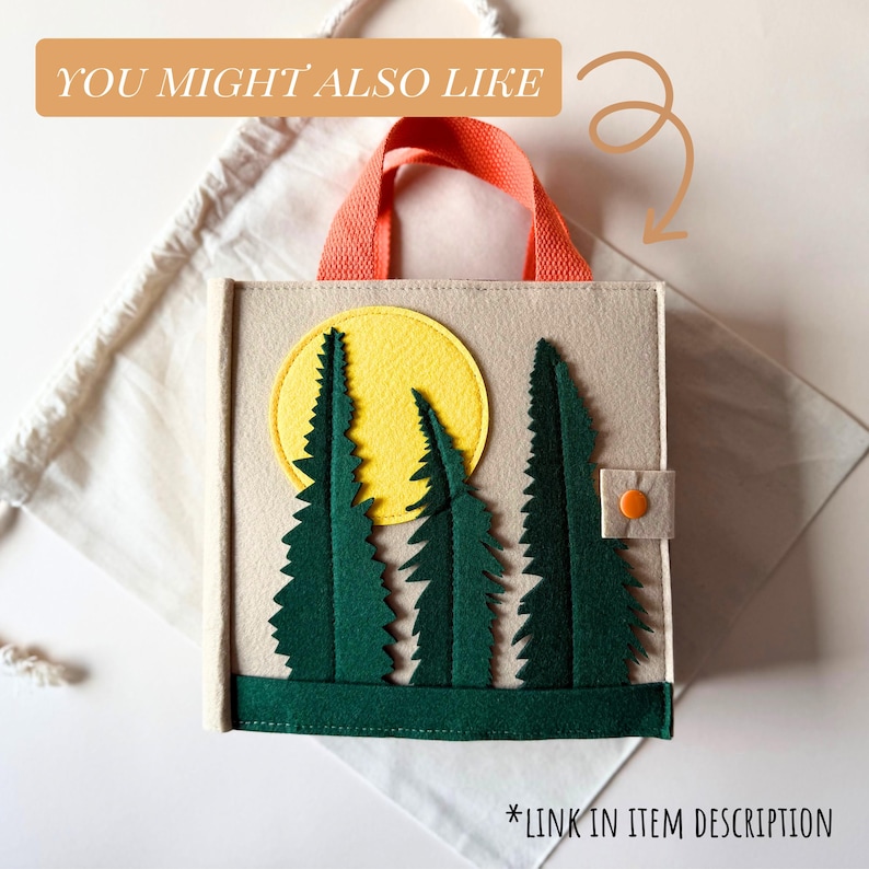 May include: A beige felt book with a forest scene featuring green trees and a yellow sun. It has an orange handle and a small orange button closure. The text "YOU MIGHT ALSO LIKE" and "*LINK IN ITEM DESCRIPTION" are visible.
