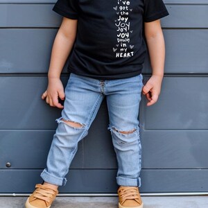 May include: Three photos of children wearing t-shirts with the text "I've got the Joy Joy Joy Down in my Heart" printed on them. The children are smiling and wearing different colored shirts. The first child is wearing a pink shirt and sunglasses. The second child is wearing a black shirt and blue jeans. The third child is wearing a navy blue shirt and blue jeans.
