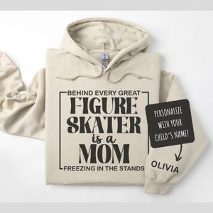 May include: A beige hooded sweatshirt with the text "Behind every great figure skater is a mom freezing in the stands". There is a white box with the text "Personalize with your child's name!" and an arrow pointing to the text "Olivia".