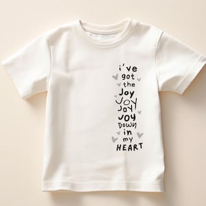 May include: A white t-shirt with short sleeves. The shirt features the text "I've got the Joy Joy Joy Joy down in my HEART" in black, with small gray hearts scattered around the text.