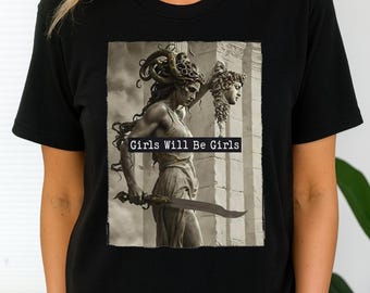May include: Black t-shirt featuring a sepia-toned graphic of a woman with Medusa-like hair holding a sword and a severed head. The text "GIRLS WILL BE GIRLS" is displayed across the image. The shirt has a crew neck and short sleeves.
