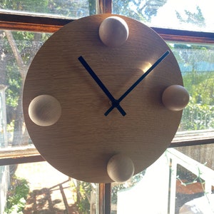 Puede incluir: Un reloj de madera con manecillas negras y cuatro pomos de madera alrededor de la esfera.