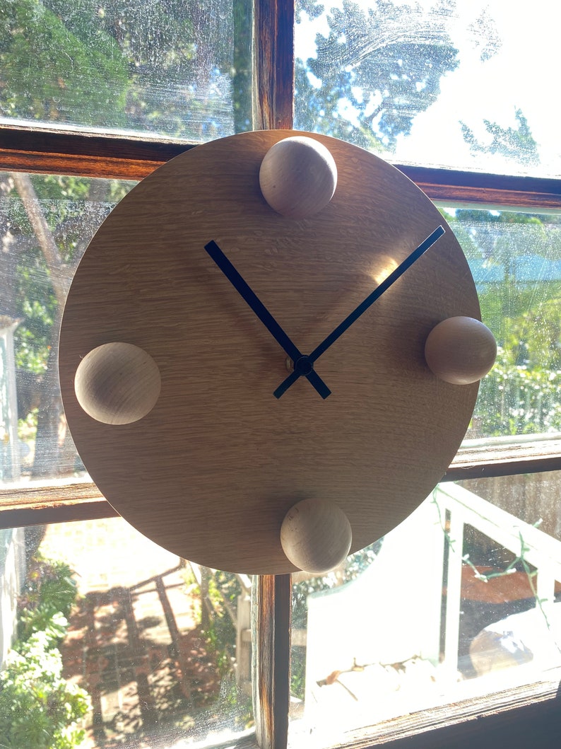Puede incluir: Un reloj de madera con manecillas negras y cuatro pomos de madera alrededor de la esfera.